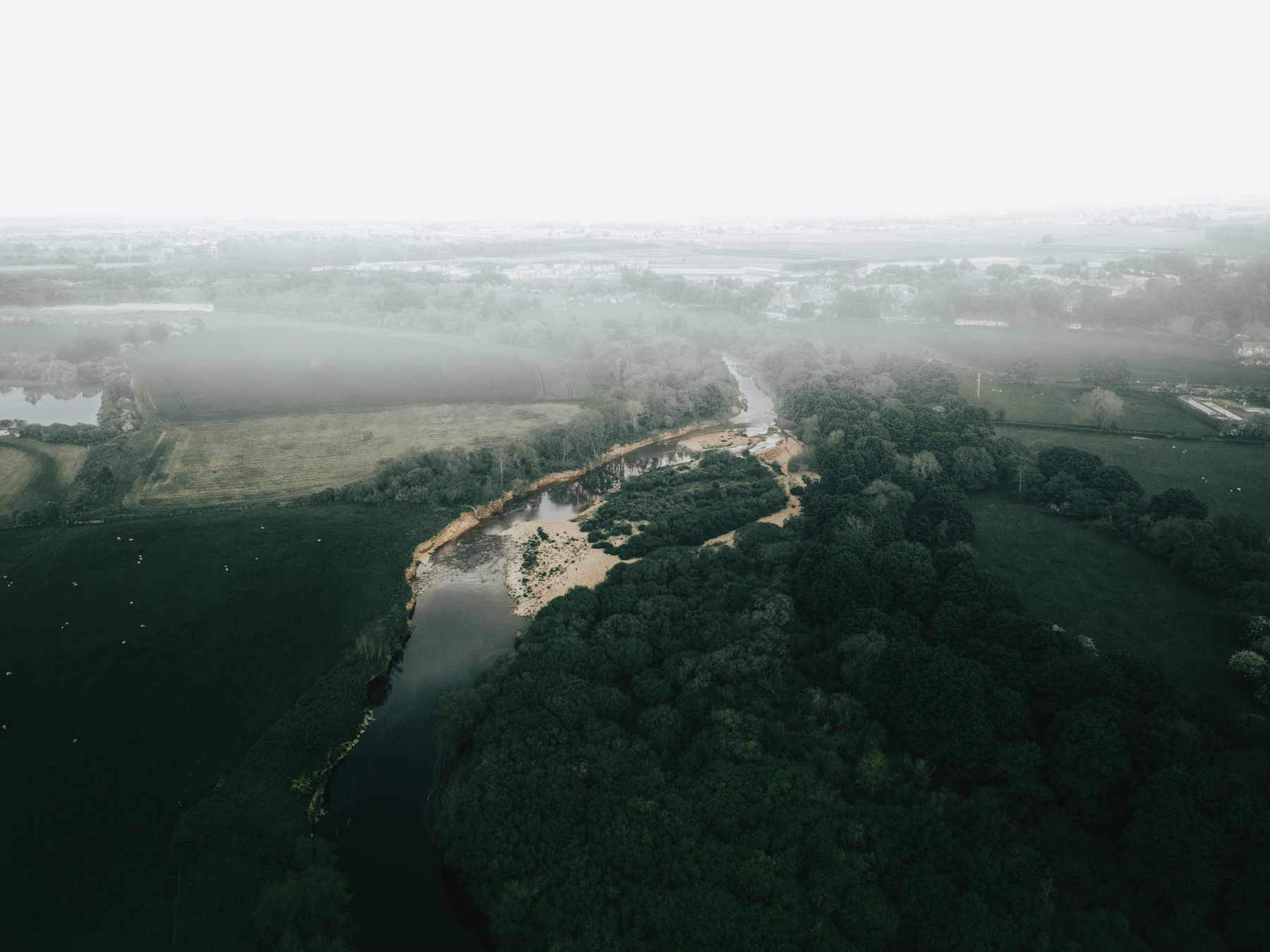 A river winding through misty English farmland, seen from the air